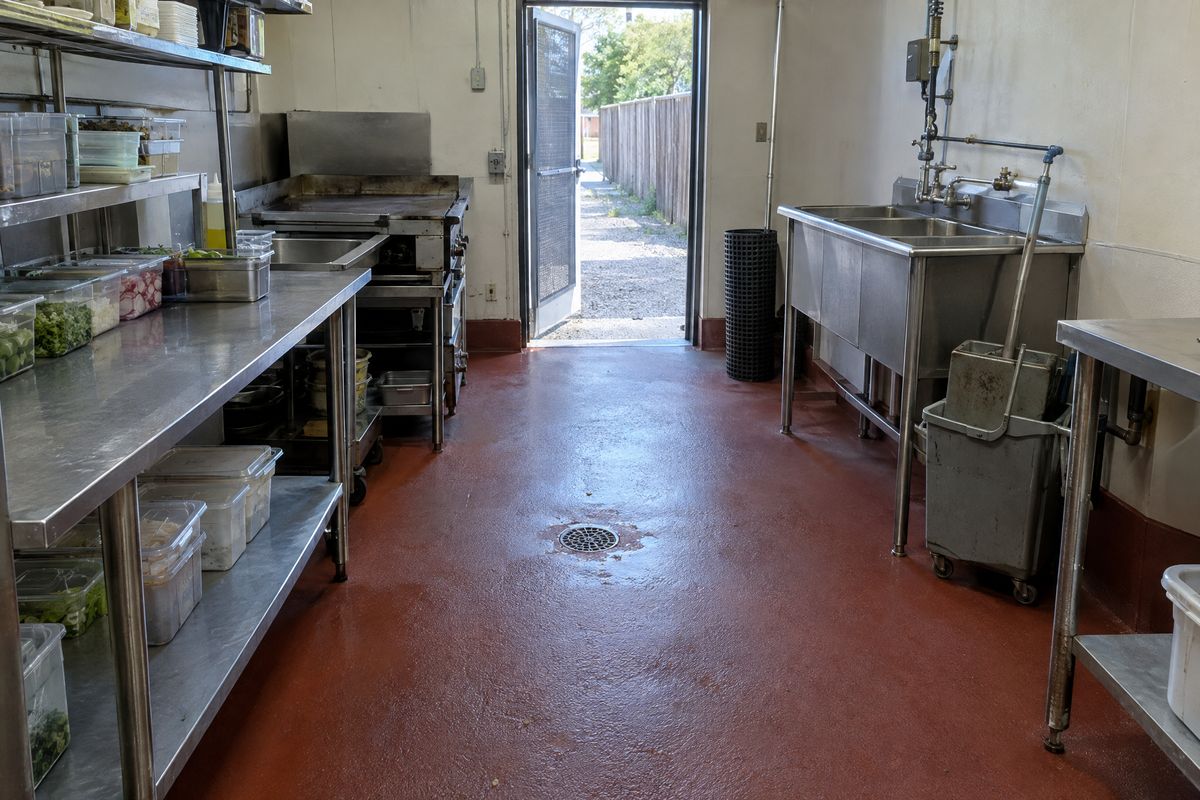 A small restaurant kitchen with a brick-red urethane cement floor, a coved base, a round floor drain, stainless prep tables, a griddle and a mop bucket